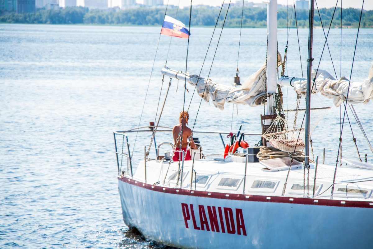 Solo sailor navigating a sailboat named Planida on a sunny day with calm waters.